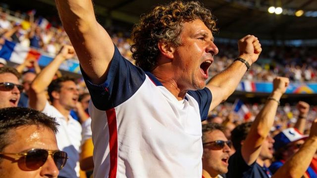 Energetic football fan cheering and raising fists in crowded sunlit stadium stands