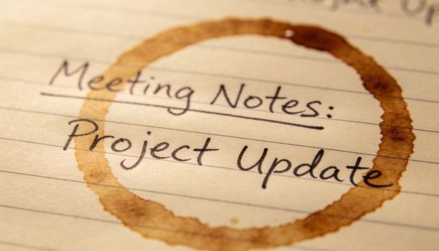 Meeting notes project update handwriting on lined notebook featuring coffee ring stain