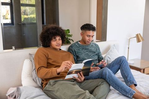 Diverse Male Friends Relaxing with Book and Phone in Modern Bedroom
