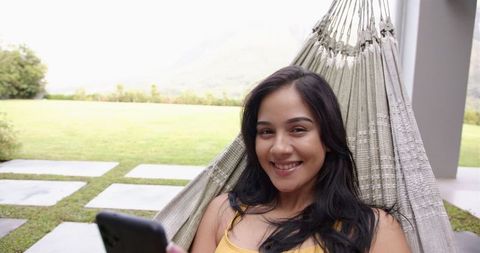 Young Woman Relaxing in Hammock with Smartphone in Backyard