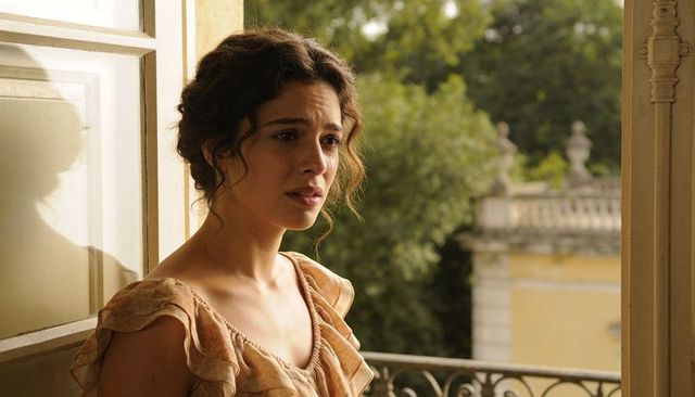 Sunlit woman crying on ornate balcony in ruffled peach dress, vintage emotional portrait