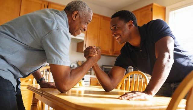 Father and adult son arm wrestling at kitchen table, friendly family competition