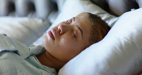 Young woman sleeping peacefully in cozy bed with white pillows tufted headboard closeup