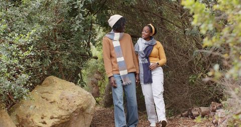 African american couple walking through autumn woodland wearing sweaters and scarves