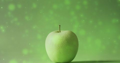 Dew-kissed green apple on glossy green backdrop