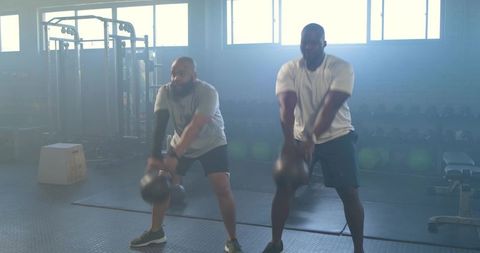 African american men swinging kettlebells during intense strength training session in gym