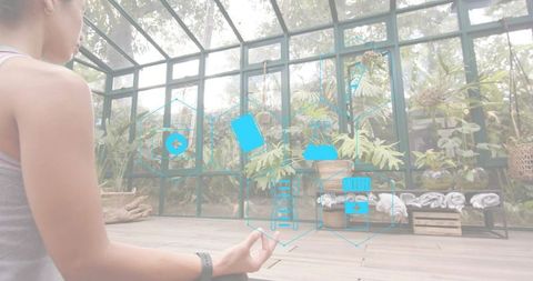 Woman meditating in sunroom wearing fitness band with augmented reality health icons