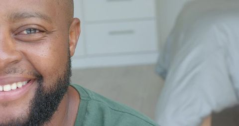 Smiling african american man wearing green crewneck in bedroom closeup with beard
