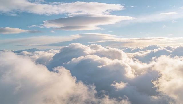 Sunlit billowy cumulus clouds with lenticular layers and golden rim light over horizon