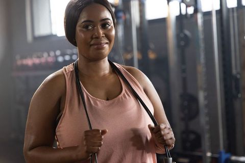 African American Woman Preparing for Workout Holding Jump Rope Near Weight Plates in Gym