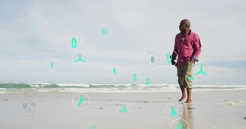 Black man walking on beach wearing pink shirt holding hat with teal icons and copy space