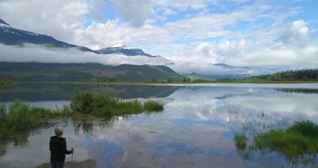 Hiker Admiring Reflective Mountain Lake with Cloudy Sky - Download Free Stock Photos Pikwizard.com