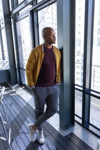 Stylish african american man leaning on balcony column overlooking urban cityscape