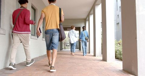 Students walking in school hallway with backpacks and books