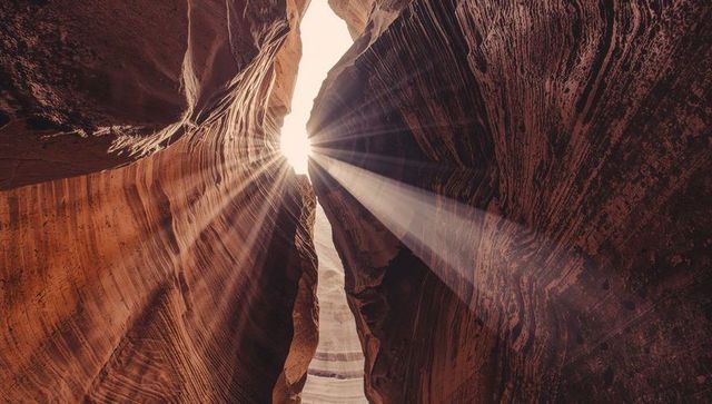 Sunbeams streaming through narrow slot canyon opening lighting striated sandstone walls