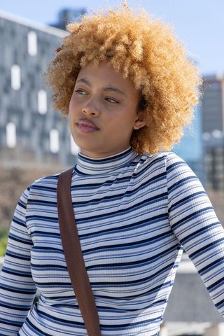 Contemplative african american woman leaning on city ledge wearing striped top, sunny urban portrait