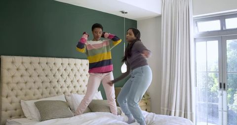 Cheerful Friends Jumping on Bed in Cozy Modern Bedroom