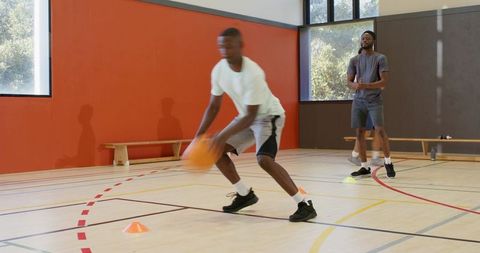 Male athletes dribbling through cones in indoor basketball agility drill training session