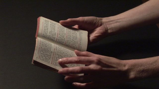 Hands holding an open religious book in dim lighting, creating a solemn and contemplative atmosphere. Ideal for use in religious contexts, studies about faith, personal inspiration themes, or materials highlighting the importance of spirituality and reading religious texts.