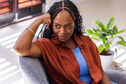 African woman relaxing on modern armchair with warm rust shirt and braided hair