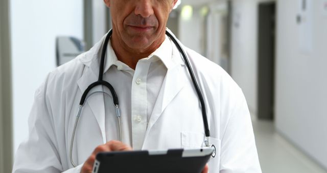 A middle-aged Caucasian male doctor reviews patient information on a digital tablet, with copy space. His focused expression and professional attire underscore the importance of accurate medical record-keeping.