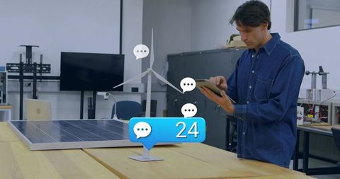 Engineer holding tablet inspecting wind turbine and solar panel prototype with 24-chat badge
