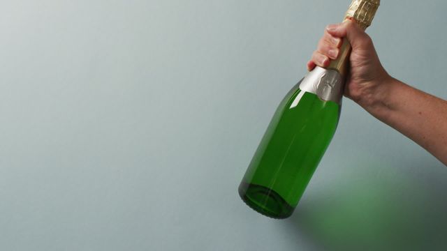 This image captures a hand firmly holding a champagne bottle against a plain backdrop. Ideal for wine brands, event invitations, and celebratory themes that require a touch of sophistication and festivity. Perfect for marketing materials, including brochures and online advertisements promoting luxury events or holiday celebrations.