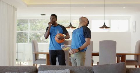 Friends wearing matching blue shirts watching basketball at home with snacks and drinks
