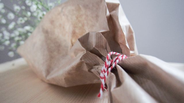 Close-up of a bouquet of flowers wrapped in brown paper and tied with decorative red and white twine. Suitable for use in themes related to gift-giving, celebrations, and minimalist floral arrangements. Great for websites, blogs, and advertising materials emphasizing natural and eco-friendly packaging.