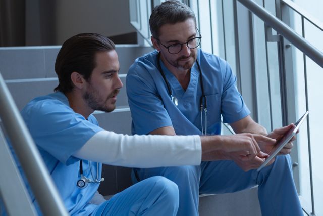 Front view of male surgeons discussing over clipboard while sitting on stairs at hospital