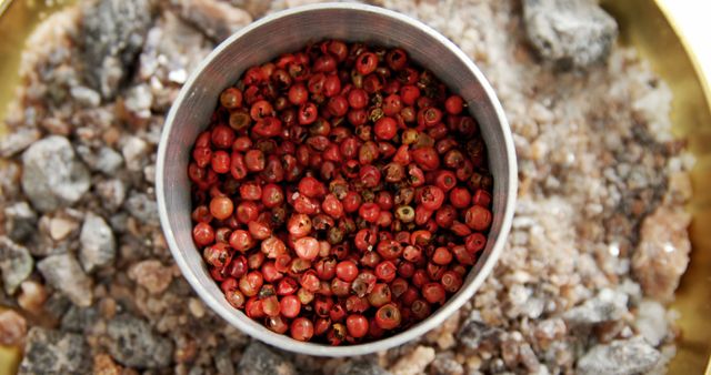 A bowl of red peppercorns is surrounded by coarse salt, presenting a vivid contrast in textures and colors. Red peppercorns add a fruity, spicy flavor to dishes and are a staple in various cuisines.