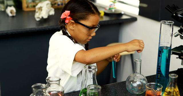 Young girl wearing safety goggles conducting a science experiment in a classroom laboratory. She is using beakers and measuring liquids, symbolizing education and the importance of STEM learning. Ideal for content related to education, science programs, classroom activities, and promoting STEM curriculum.