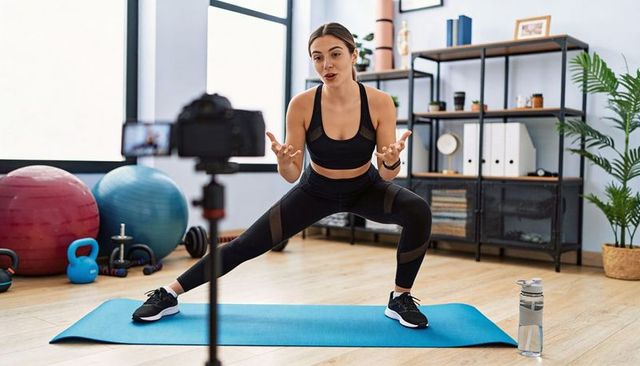 Female fitness coach recording lateral lunge tutorial in home gym for online workouts
