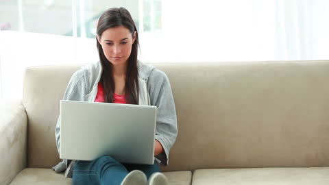 Focused Young Woman Using Laptop on Sofa at Home