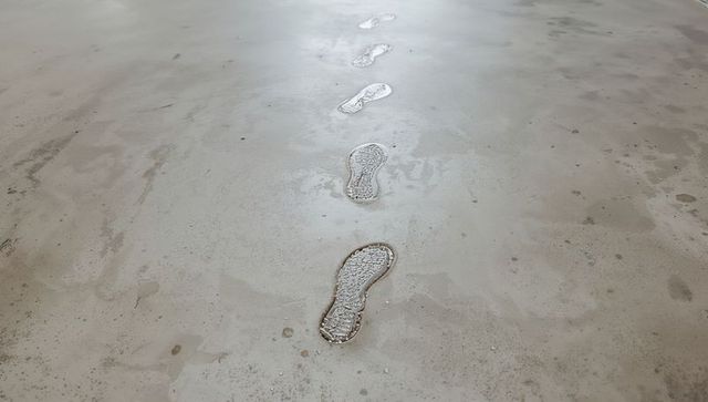 Wet shoe footprints leading across stained concrete floor with puddles and tread marks