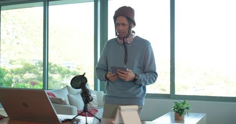 Content creator standing in home office holding tablet wearing beanie and headphones