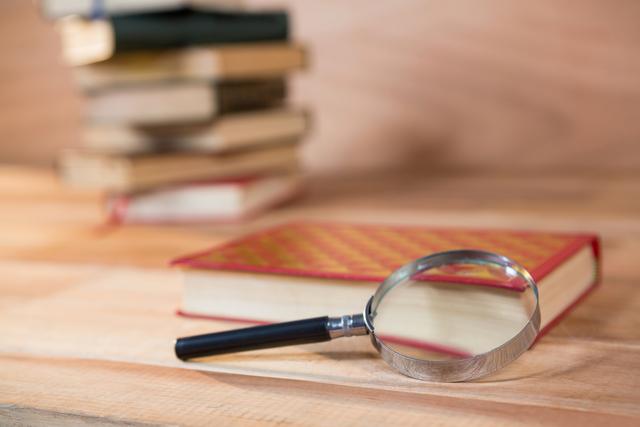 Magnifying glass placed next to a book on a wooden table, ideal for themes related to reading, research, and education. Suitable for use in articles, blogs, and websites focusing on literature, study tips, and academic resources.