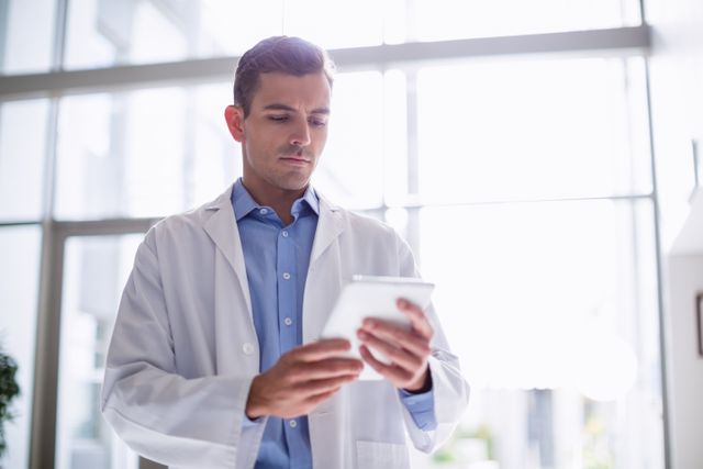Doctor using digital tablet in corridor at hospital