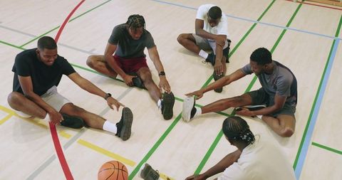 Diverse male athletes stretching in gym circle warming up for basketball teamwork