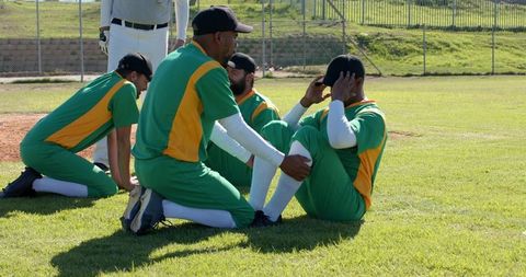 Diverse baseball teammates warming up and stretching on grass near infield dirt before game