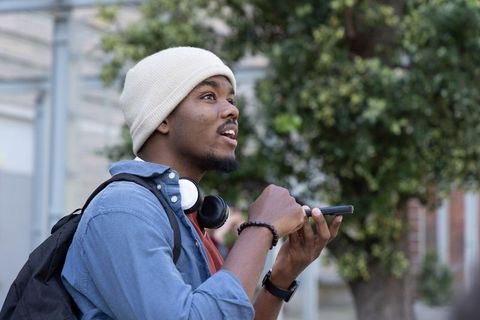 African american man using smartphone with headphones and backpack on urban sidewalk