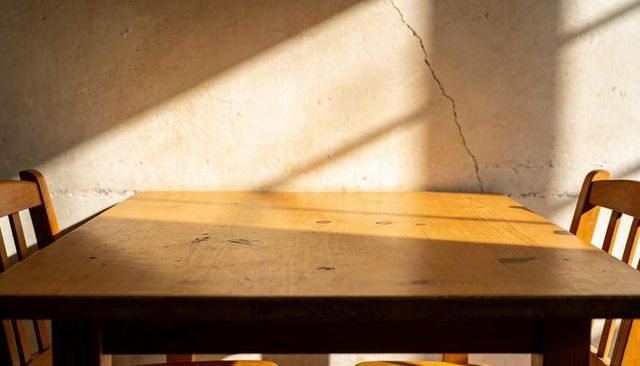 Wooden Dining Table Basking in Warm Sunlight with Rustic Plaster Wall Crack