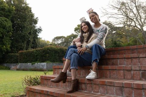 Multicultural women hugging on steps wearing cozy sweaters, jeans and holiday headbands