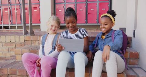 Diverse Group of Smiling Schoolgirls Using Tablet on School Steps