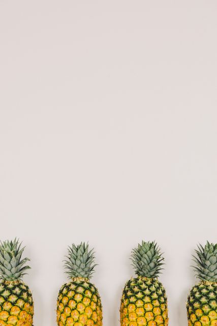 Four ripe pineapples lined up in a row against a minimalist beige background. Great for use in advertisements, healthy living and organic food promotions, tropical vacation themes, or any content related to fresh produce and clean eating.
