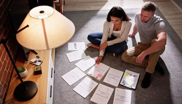 Couple sorting bills and reviewing charts on living room floor planning household budget