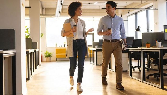 Young professionals walking and chatting with coffee in bright open-plan office space