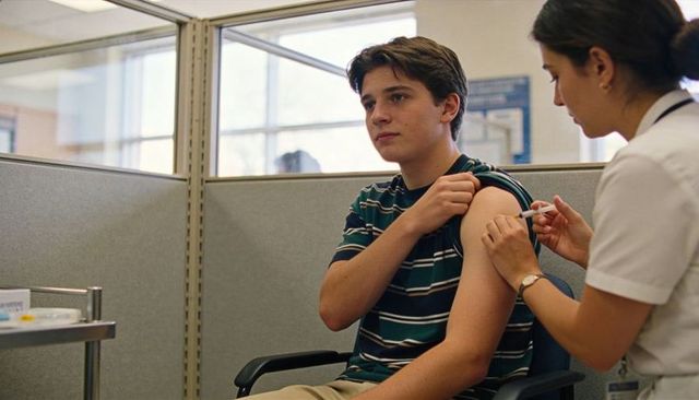 Teen receiving vaccine from nurse in clinic cubicle during routine health visit
