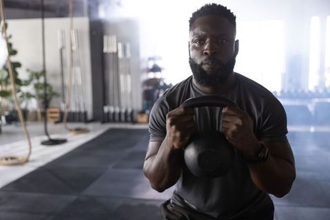 African American man holding kettlebell performing goblet squat in modern gym, focused