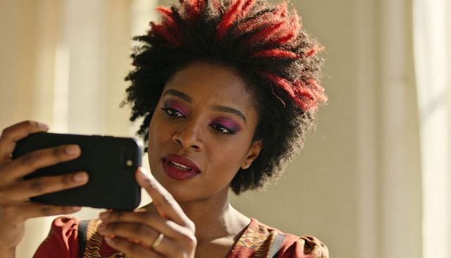 Black woman holding smartphone and checking messages with bold purple makeup and patterned top